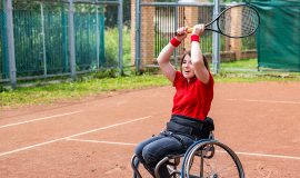 A disabled young woman in a wheelchair playing tennis on a tennis court.