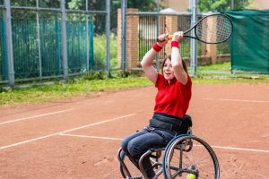 A disabled young woman in a wheelchair playing tennis on a tennis court.
