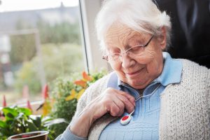 Elderly lady sat at home admiring her personal alarm pendant hanging from her neck