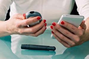 Woman using phone and blood glucose meter to manage diabetes treatment